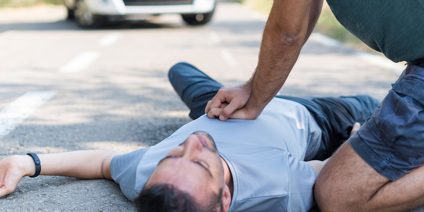 Ein Mann liegt auf dem Rücken auf der Straße. neben ihm kniet ein Mann und führt eine Herzdruckmassage durch.
