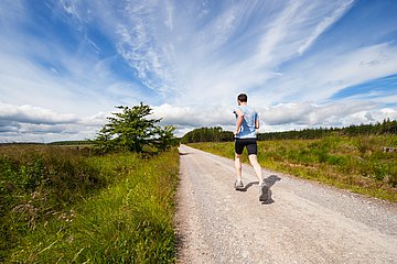 Läufer Ein Jogger läuft auf einem Feldweg in die weite Landschaft hinein.