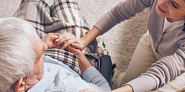 Foto: Eine j&uuml;ngere Frau sitzt neben einem &auml;lteren Mann und h&auml;lt seine Hand.