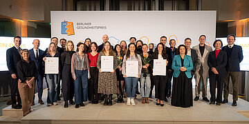 Die Gewinnerinnen und Gewinner des Berliner Gesundheitspreises stehen auf der B&uuml;hne zusammen mit Dr. Carola Reimann, Vorstandsvorsitzende des AOK Bundesverbandes und Dr. Peter Bobbert, dem Pr&auml;sidenten der &Auml;rztekammer Berlin und halten ihre Urkunden in den H&auml;nden.