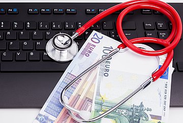 Positiver Jahresabschluss 2022 Auf einer Tastatur liegen Geldscheine und ein Stethoskop
