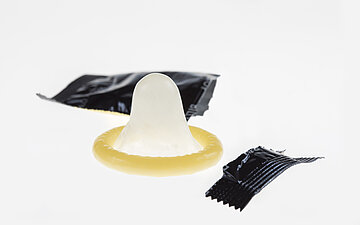 Ein Kondom liegt zwischen den Teilen einer auseinander gerissenen Verpackung.