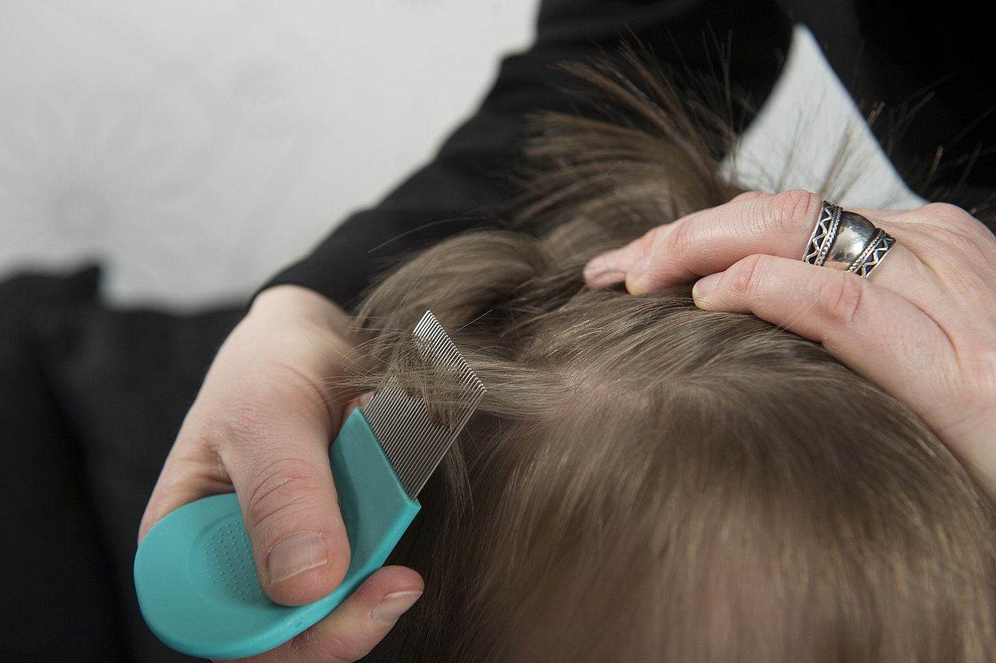 Das Foto zeigt einen Kinderkopf in Nahaufnahme. Eine Frau sucht die Haare des Kindes mit einem Nissenkamm nach Läusen ab.