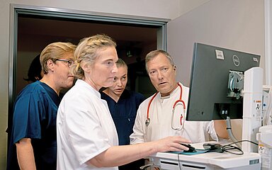 Mehrere medizinische Fachkr&auml;fte stehen vor einem Computer und besprechen gemeinsam die Patientendaten auf dem Bildschirm.