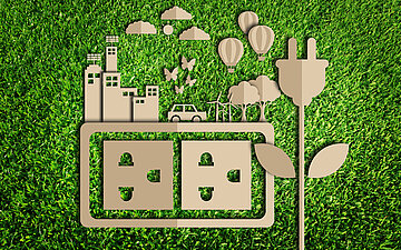 Illustration: Zu sehen sind verschiedene Scherenschnitte von Symbolen, die Bestandteile einer Kommune darstellen, wie H&auml;user, ein Auto, Windr&auml;der und B&auml;ume, in brauner Farbe vor dem Hintergrund einer gr&uuml;nen Wiese. Darunter sind symbolhaft zwei Steckdosen sowie daneben ein Stecker in Form einer Blume zu sehen.