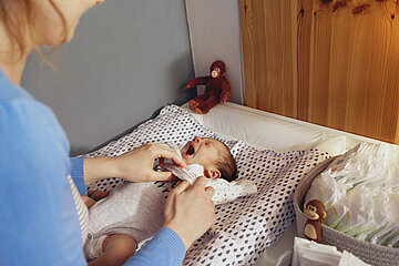 Ein Neugeborenes liegt auf einem Wickeltisch und wird gewickelt.