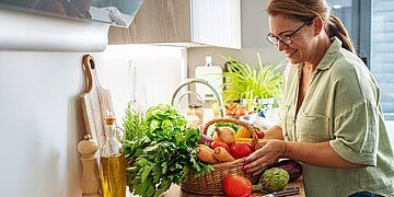 Eine Frau steht vor einem Korb mit Gem&uuml;se.