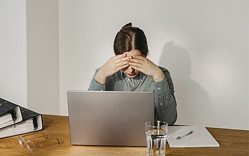 AU-Bericht Eine Frau sitzt vor einem Notebook. Sie wirkt erschöpft.