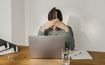 AU-Bericht Eine Frau sitzt vor einem Notebook. Sie wirkt erschöpft.