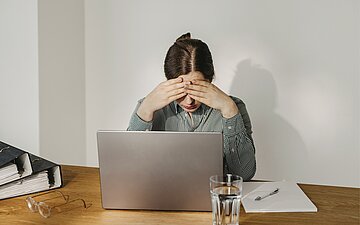 Eine Frau sitzt vor einem Notebook. Sie wirkt ersch&ouml;pft.