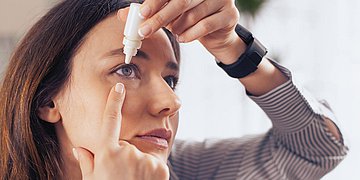 Augentropfen Foto: Eine junge Frau tropft sich Augentropfen in die Augen.