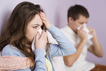 Volle Wartezimmer Zwei Patienten sitzen im Wartezimmer einer Arztpraxis und schnäuzen in Taschentücher.