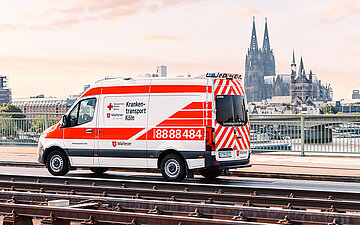 Foto eines Krankenwagens, der vor einer Stadtsilhouette &uuml;ber eine Br&uuml;cke f&auml;hrt