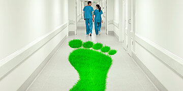 Foto: Ein Krankehausflur mit zwei Pflegenden von hinten und einem gro&szlig;en gr&uuml;nen Fu&szlig;abdruck auf dem Fu&szlig;boden.