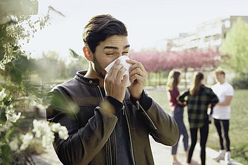 Ein Mann steht im Park und putzt sich die Nase