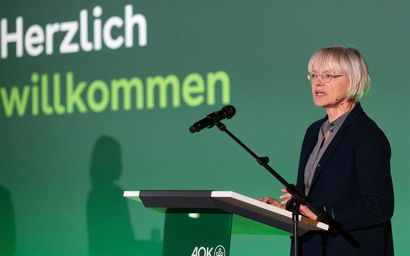 Eine Frau hält eine Rede hinter einem Rednerpult. 