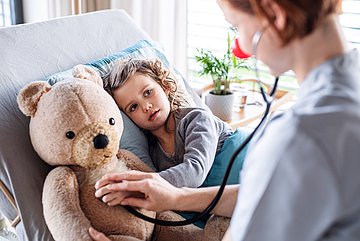 Krankenhausbehandlungen von Kindern Kind liegt im Krankenhausbett. Die Ärztin untersucht zuerst ihren Teddy.