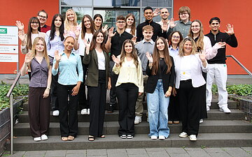Gruppenfoto mit den neuen Azubis der AOK Mittlerer Oberrhein auf einer Treppe vor einem AOK-Geb&auml;ude.
