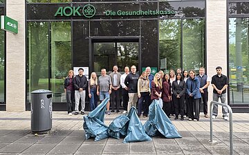 Am World Cleanup Day 2026 steht das Team Stuttgart mit M&uuml;lls&auml;cken vor dem AOK-Geb&auml;ude.