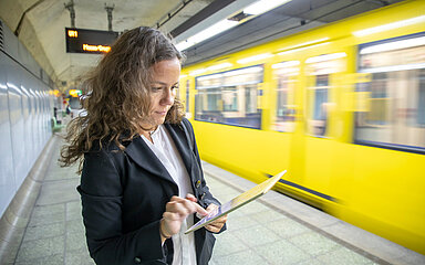 Eine Frau checkt ihre E-Mails auf einem Tablet am U-Bahnsteig.