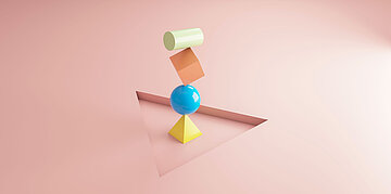 Auf einem rosanen Boden steht eine Balance-Figur aus verschiedenfarbigen Formen (Kugel Zylinder, W&uuml;rfel, Pyramide).