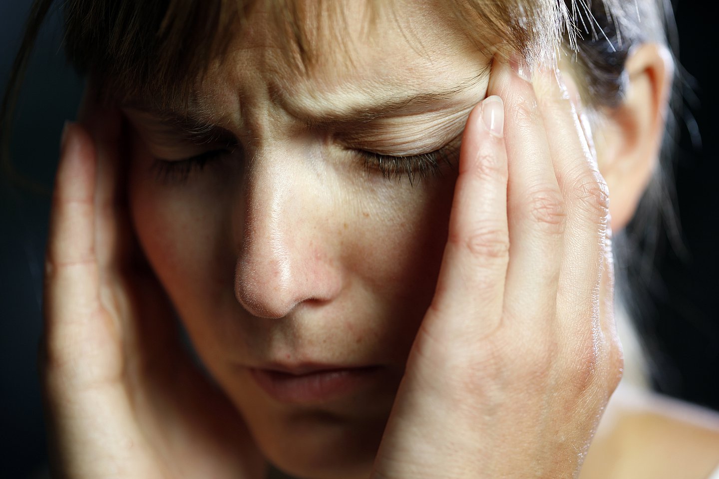 Foto: Eine junge Frau fasst sich an den Kopf. Sie leidet unter Kopfschmerzen.