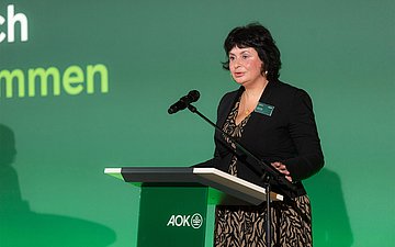 Eine Frau hält eine Rede hinter einem Rednerpult.