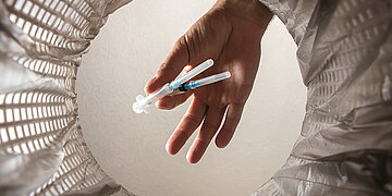 Foto einer Hand, die benutzte Spritzen in einen M&uuml;llbeh&auml;lter wirft.