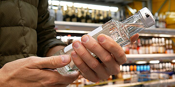 Person, die im Supermarkt eine Flasche mit hochprozentigem Alkohol in den H&auml;nden h&auml;lt und darauf blickt