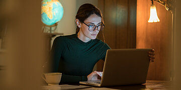 Eine junge Frau sitzt am Schreibtisch vor einem Laptop