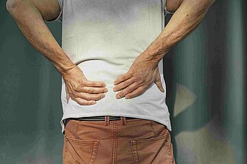 Ein Mann reibt die H&auml;nde an seinem R&uuml;cken, weil er Schmerzen hat.