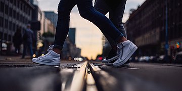 Foto: Füße in Turnschuhen, die über eine Straße gehen.