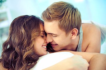 Sexuell übertragbare Krankheiten verursachen oft keine Beschwerden Foto: Ein junges Paar liegt im Bett aneinander gekuschelt.