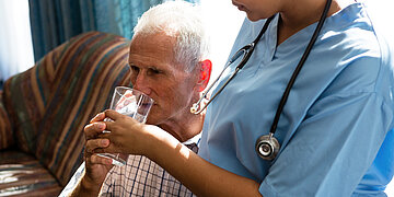 Pflegekraft hilft Pflegebed&uuml;rftigem beim Wassertrinken.