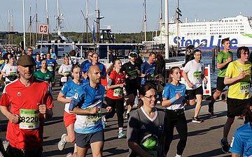 Zahlreiche L&auml;uferinnen und L&auml;ufer laufen bei bestem Wetter entlang der Kiellinie, im Hintergrund sind Boote zu sehen.