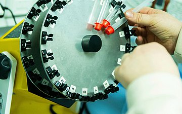 Blick auf einen Rotator zur Durchmischung von Wasserproben, in den jemand von Hand Proben einsteckt