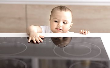 Kindersicherheit Foto: Kleinkind fasst auf Bedienfeld von Herdplatte.