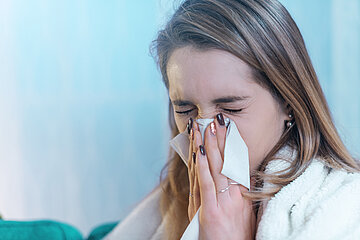 Eine junge Frau in Nahaufnahme schn&auml;uzt sich die Nase.