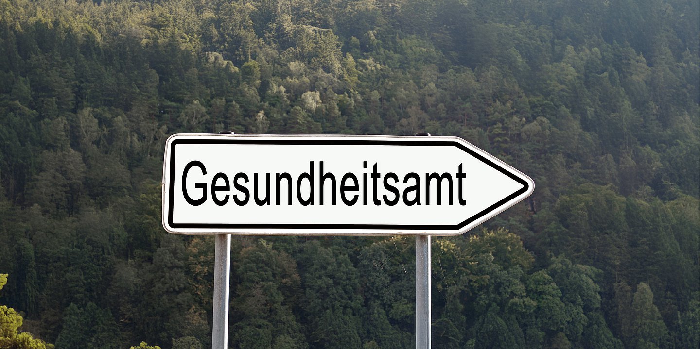 Foto: Ein weißes Straßenschild zeigt nach rechts, darauf der Schriftzug "Gesundheitsamt".