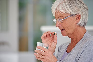 Foto PM Antibiotika-Verbrauch in Bayern unter dem Niveau vor der Pandemie Schmuckbild zeigt eine Frau die mit Hilfe eines Glases Wasser eine Pille schluckt