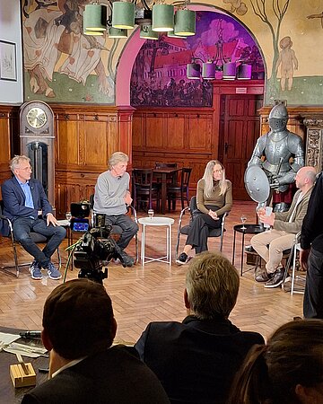 Teilnehmer des TV-Talks zum Thema "Longevity" sitzen auf der B&uuml;hne und diskutieren vor Publikum.