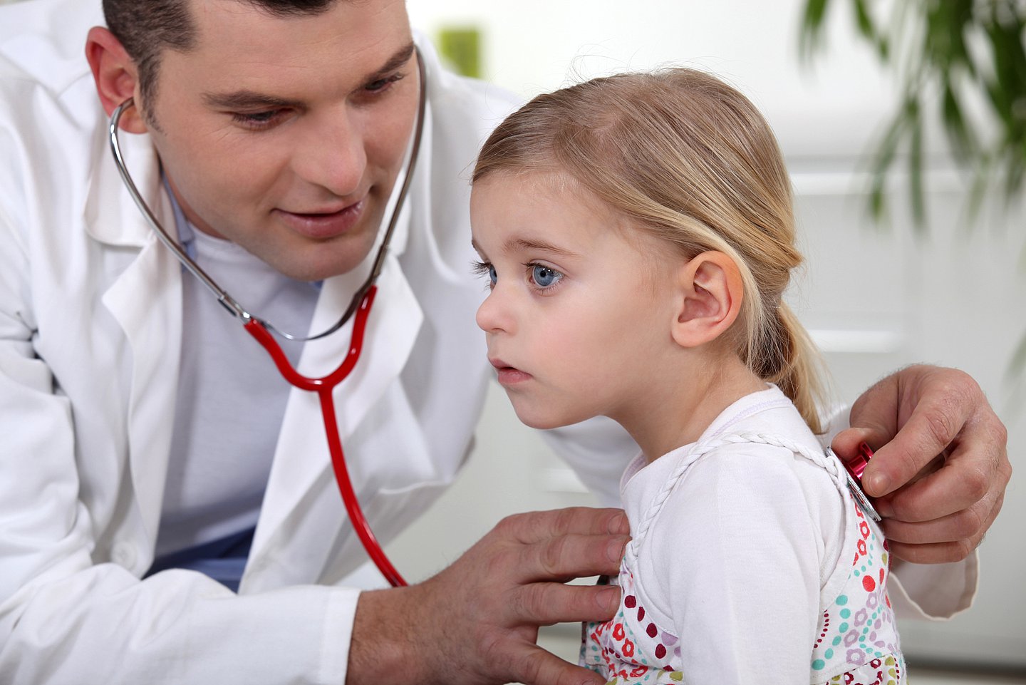 Ein Arzt hört in der Praxis ein kleines Mädchen mit dem Stethoskop ab.