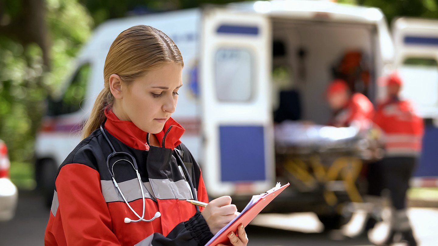 Foto zeigt eine Notärztin, die nach einem Einsatz etwas auf einen Klemmbrett notiert. 