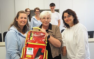 Marina Schiele (l.) erh&auml;lt von Petra Hieber von der AOK Ostw&uuml;rttemberg f&uuml;r ihre T&auml;tigkeit als VERAH einen entsprechenden VERAHmobil-Rucksack ausgeh&auml;ndigt. Dr. Sandra Esber-Schimmel (r.) und Hintergrund ihr Praxisteam &ndash; mit der 2. VERAH Nicole Geist und Medizin Student Marlon Trost &ndash; freuen sich. 