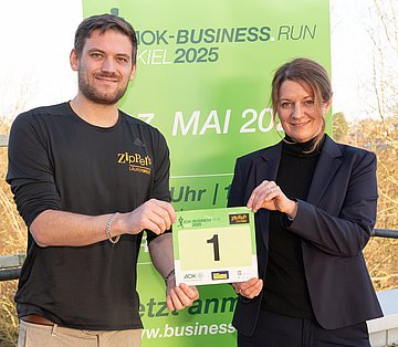 Vorankündigung des ‚AOK-Business.Run Kiel‘ für 2025Vorankündigung des ‚AOK-Business.Run Kiel‘ für 2025 Ein junger Mann und eine Frau stehen vor einem Roll-up, auf dem die Daten des Laufs vermerkt sind und halten beide gemeinsam die Startnummer "1" in der Hand.