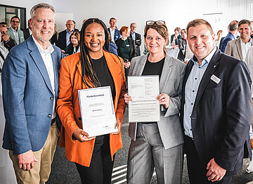 Die genannten Personen stehen zusammen im Veranstaltungsraum. Die Ministerin h&auml;lt den Forderbescheid in den H&auml;nden, die AOK-Landesdirektorin das Anschreiben dazu.