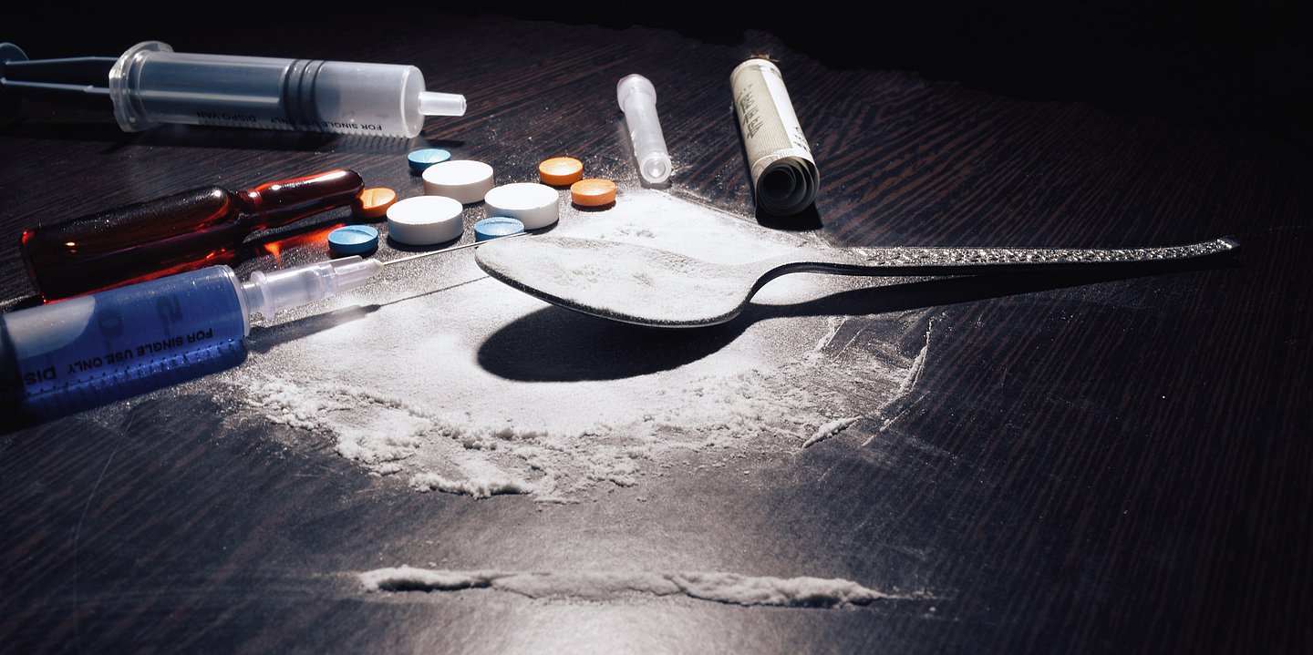 Auf einem Tisch liegen ein Löffel mit weißen Pulver, eine Spritze und weitere Utensilien für den Drogenkonsum.
