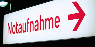 Notaufnahme Ein Wegweiser-Schild mit roter Leuchtschrift "Notaufnahme" und einem Pfeil nach rechts.