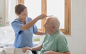 Pflege Foto eines alten Mannes, dem in einem Bad die Haare gekämmt werden