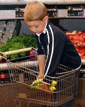 Junge kauft ein In einem Supermarkt legt ein Junge Waren in einen Einkaufswagen.